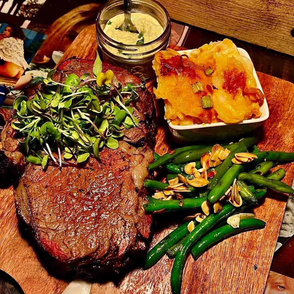 Grilled steak with microgreens, potato gratin, green beans, almonds, and a side of sauce.