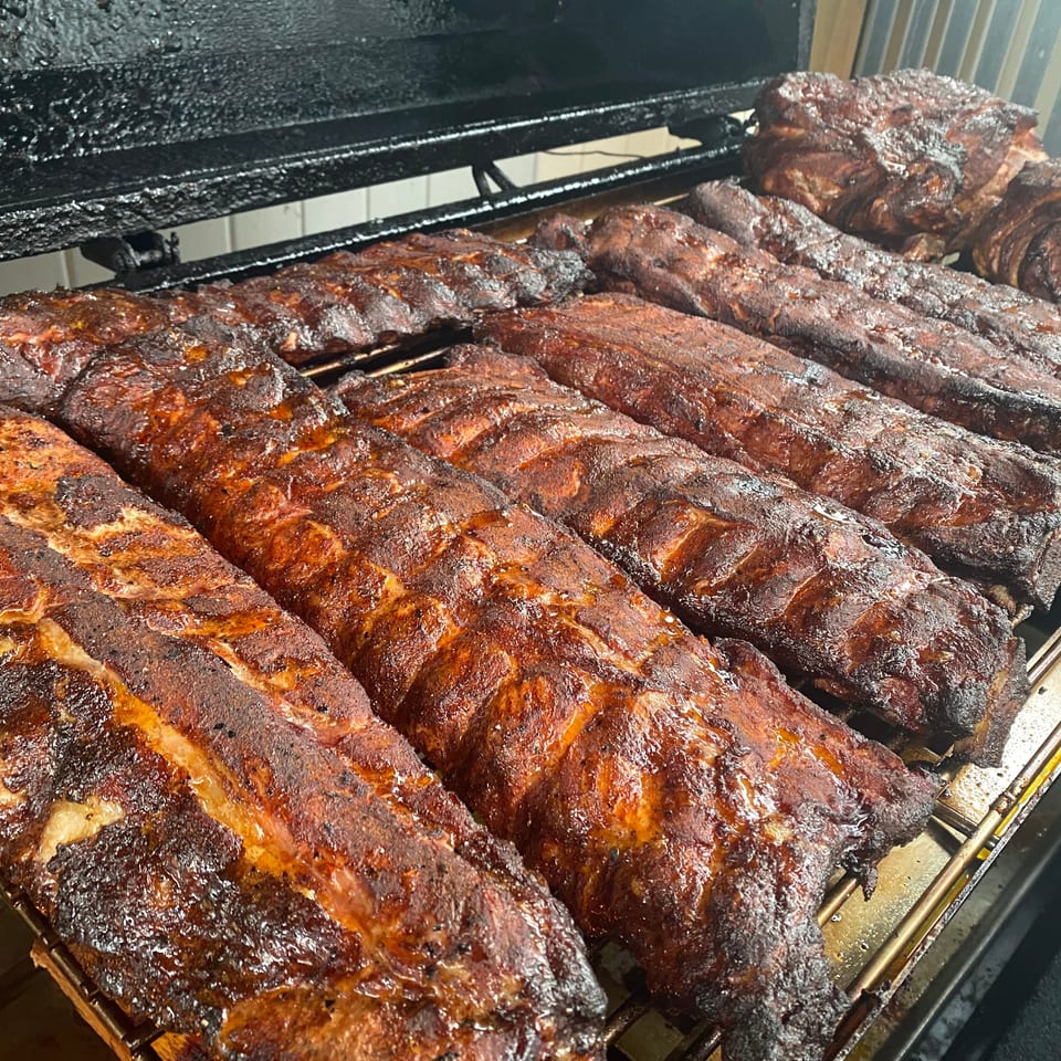 Rows of glazed, smoky barbecue ribs cooking on racks inside a commercial smoker.
