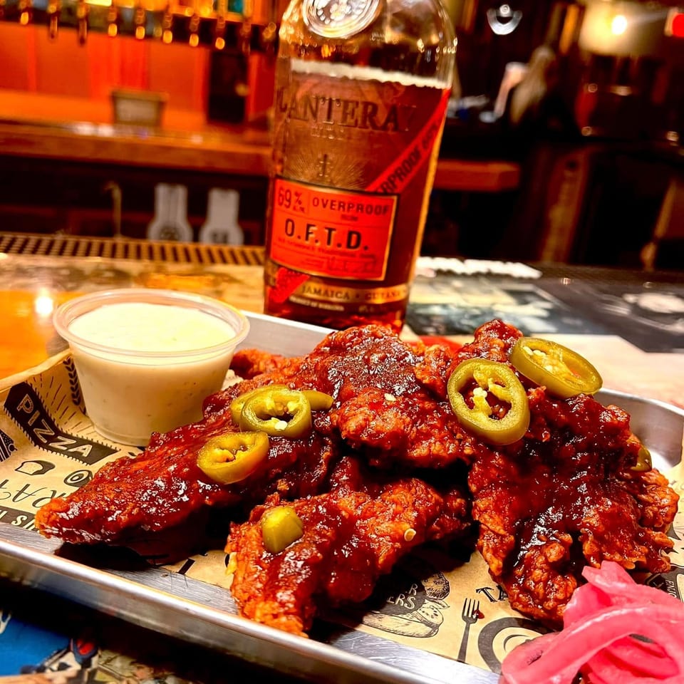 Spicy chicken wings with jalapeños and pickled onions, with a bottle of rum in the background.