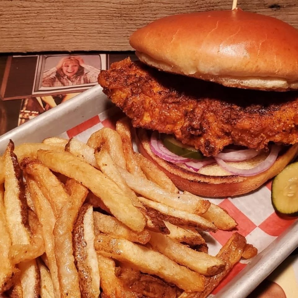 Crispy fried chicken sandwich with pickles, red onion, and a side of golden french fries.