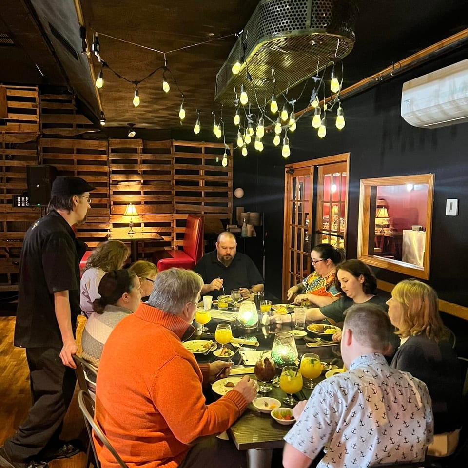 A group of people dining at a long table in a dimly lit restaurant with string lights.