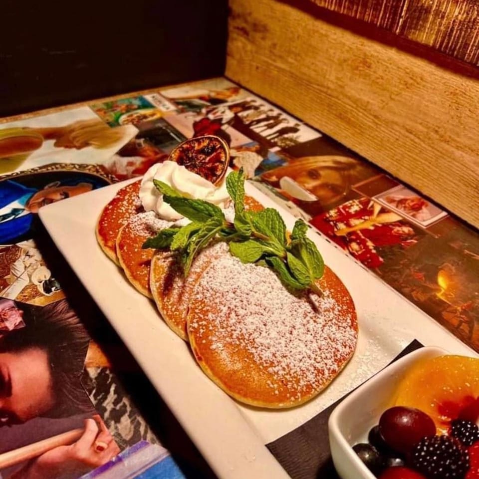Fluffy pancakes with powdered sugar, whipped cream, mint, and a side of fresh fruit.